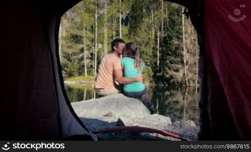 Outdoors activities and young people in nature, man and woman camping with tent near mountain lake, viewed from inside tent. Dolly shot