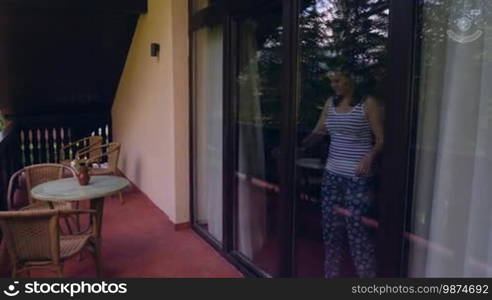 Pan of young woman coming on terrace to relax in the morning. Woman awakened from sleep breathing fresh air on villa balcony in summer.