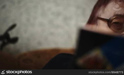 Panning close-up shot of elderly woman in glasses reading a book in the lamplight