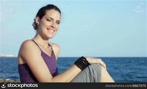 Panning on attractive young Caucasian woman looking at the sea and smiling. Copy space