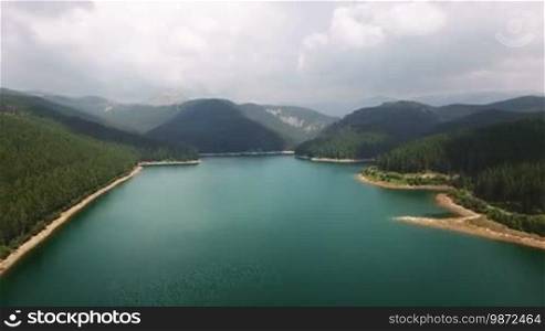 Panoramic aerial view of a lake among the forests and mountains in Romania in summer day. 4K footage. Traveling and beauty in nature concept.