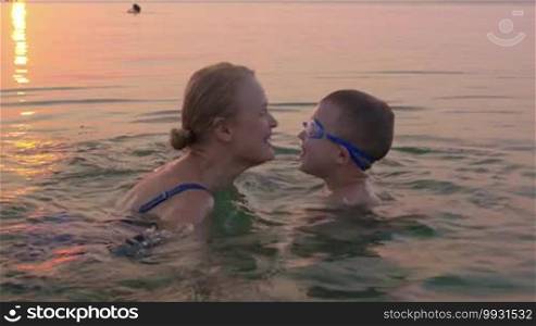 Parents and children love expression. Mother and son exchanging hugs and kisses while swimming in the sea at sunset. Family summer vacation
