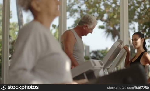 People and sports, young woman working as a personal trainer and helping a senior couple exercising in a wellness club