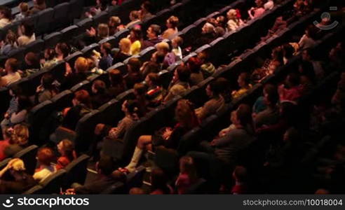 People at the theatre performance. Shot from back, no visible faces. High angle.