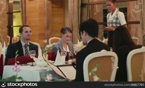 People eating, dining at hotel restaurant, leisure and fun, men and women, businessmen and wives having business dinner, talking and laughing. Asian waitress at work, taking order.