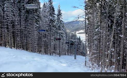 People going up on hoist through dark forest above snow winter mountains