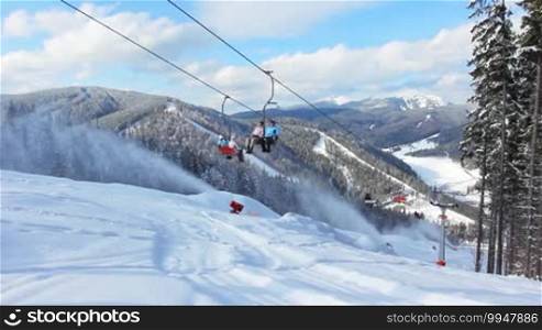 People move on a hoist, below a snow gun shoots at winter mountains