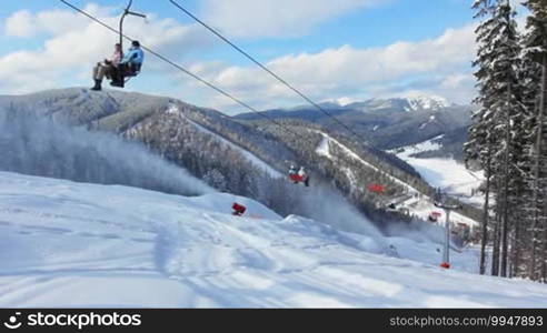 People move on a hoist, below a snow gun shoots at winter mountains, timelapse