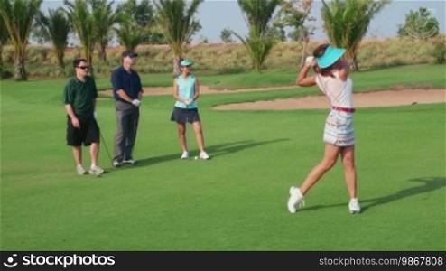 People, sport, leisure activities, recreation and lifestyle, golf in country club during summer holidays. Asian woman playing golf near hole, group of friends watching. 10 of 30