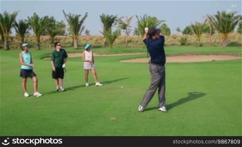 People, sport, leisure activity, recreation and lifestyle, golf in country club during summer holiday. Man playing golf near hole, group of friends watching. 9 of 30