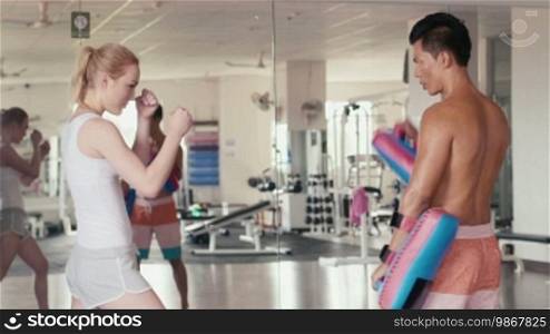 People training, working out, exercising in gym and fitness club, sport and martial arts. Personal trainer and student, man teaching boxing to woman for self-defense. Portrait looking at camera. 22 of 29