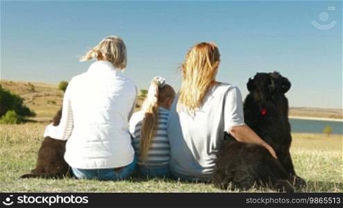 People with Newfoundland dogs resting in nature, rear view