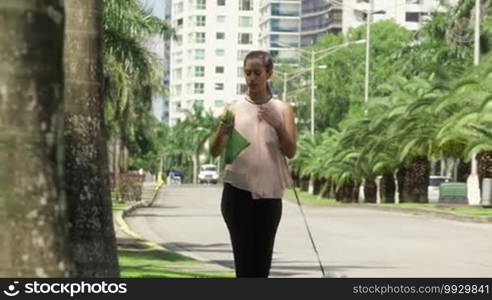 People working as dog-sitter, girl with French poodle dog in park. The young Hispanic woman picks up her pet's poo with plastic bag