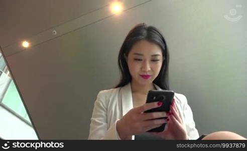 People working in hotel lobby, office building. Japanese female manager. Asian businesswoman, girl, woman at work, using mobile phone, telephone, smartphone for email, internet. Low angle