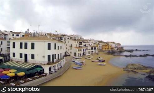 Picturesque Mediterranean fishing village in La Costa Brava, Girona. Aerial drone shot flying over the rooftops to the old center of Calella de Palafrugell. Flying over turquoise beaches with a DJI Phantom multicopter, a GoPro Hero 3 Black Edition, and an Arris gimbal. Typical Mediterranean landscape with white houses, tile roofs, wooden boats, and pristine beaches.