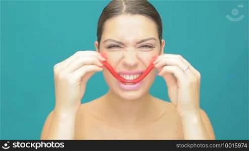 Playful woman with red jelly stretching it into a mock smile on a blue studio background
