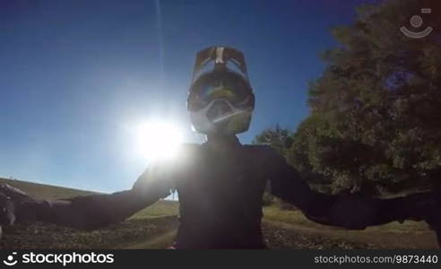 Point of View: Enduro rider in motorcycle protective gear riding bike on dirt track against the sun