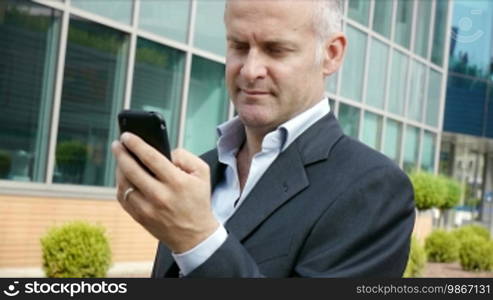 Portrait of a happy businessman with a mobile telephone, typing and browsing the internet, and looking at the camera