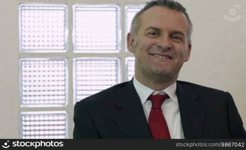 Portrait of a mid-adult male manager smiling and looking at the camera in the office. Dolly shot