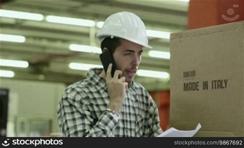 Portrait of a young man employed in a logistics facility talking on a mobile phone, people working in a warehouse, workers in the industry. 18 of 19