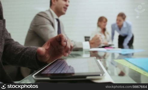Portrait of African American man writing on digital tablet PC with business people working and talking during meeting in office room. Sequence, 6 of 20