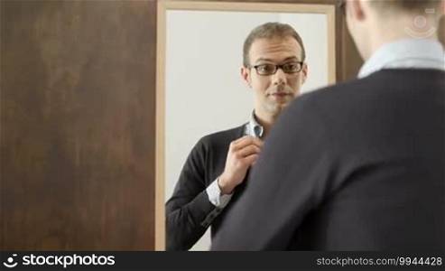 Portrait of happy young man with glasses getting ready, dressing up and smiling, looking at mirror in fashion store