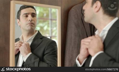 Portrait of male customer in clothing shop trying out new suit and shirt and looking at mirror