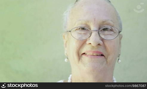 Portrait of senior Caucasian woman looking at camera against green wall and smiling