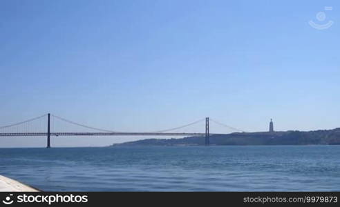 Portugal - the River Tagus in Lisbon with the Ponte 25 de Abril bridge and the Christ the King monument in the mountains under a blue sky
