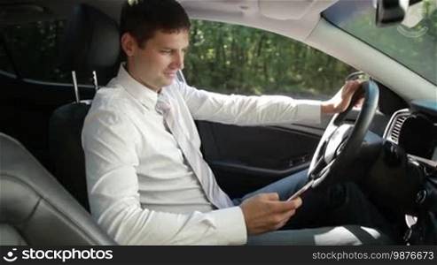 Positive young business executive browsing the net on a mobile phone while sitting in a luxury car. Side view. Smiling businessman texting on a smartphone while traveling to work by car. Slow motion. Steadicam stabilized shot.