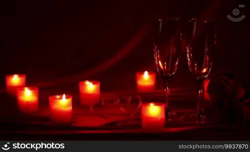 Pouring champagne in glasses at Valentine's Day celebration, still life with candles, roses, and hearts on red silk