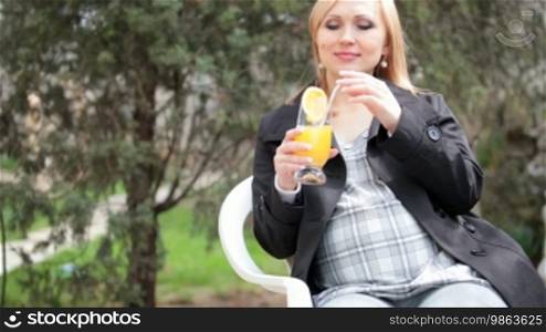 Pregnant woman drinking orange juice while sitting outdoors