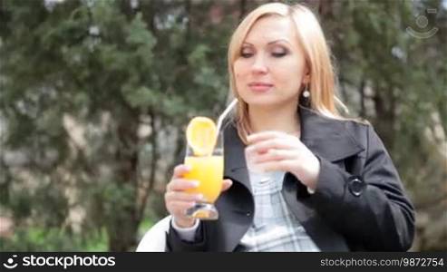 Pregnant woman drinking orange juice while sitting outdoors