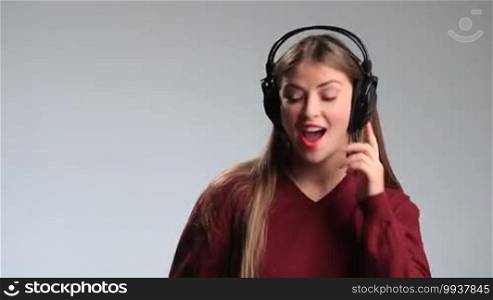 Pretty teenage girl touching headphones on her head with a happy smile on white. Excited young brunette woman in big earphones dancing, swaying along with music and relaxing.