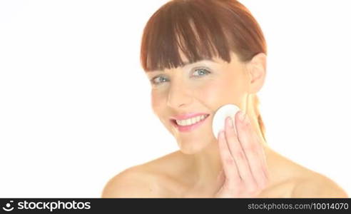 Pretty young redhead woman using a cotton pad to clean her face in a personal hygiene and skincare concept