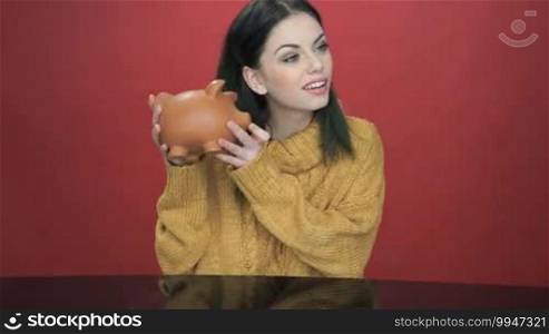 Pretty young woman shaking her piggy bank as she tries to decide if there is enough money inside to fulfill her dreams