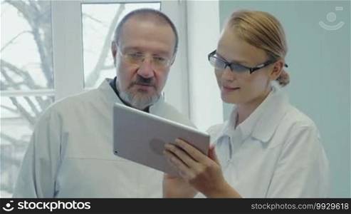Professor and young female doctor having a conversation using a digital tablet. They are discussing something shown on the tablet and reaching an agreement.
