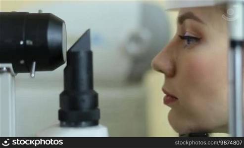 Profile of a pretty woman examining eyesight with a slit lamp by an optometrist at an eye clinic. A beautiful female patient checking vision with a virtual laser in a modern ophthalmology clinic close-up. Eye care concept.