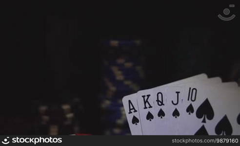 Royal flush on cards and poker chips on red casino table.