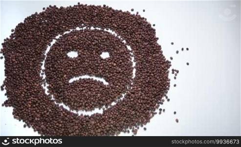 Sad emoticon made of coffee beans smiling with a cup of hot coffee on white background