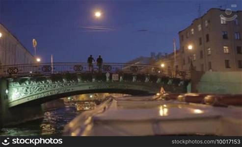 Sail on river boat in Saint Petersburg at white nights, across the Fontanka river. Two men stay on the bridge.