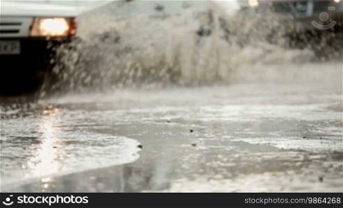 Sedan plows through a large puddle on a flooded street making splash