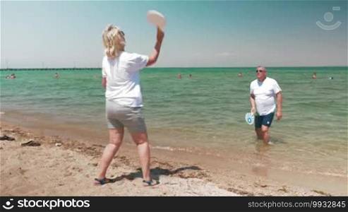 Senior adults playing badminton on sunny beach.