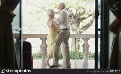 Senior Caucasian wife and husband on vacation, dancing on terrace in hotel