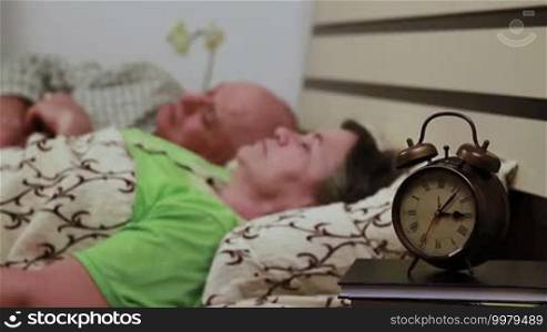 Senior couple laying in bed and peacefully sleeping. Focus on watch.
