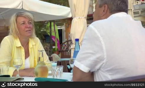 Senior man and woman in an outdoor cafe on a summer day. They are having a lovely talk and holding hands gently. People in love