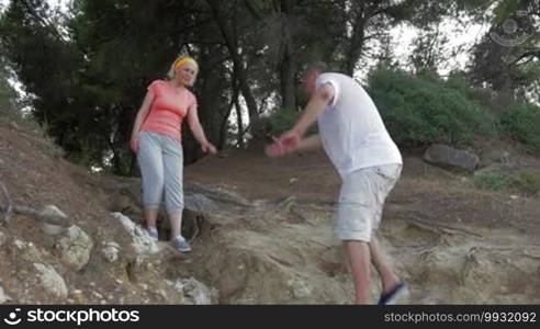 Senior man helping woman to get over heavy-going way down during outdoor hiking or training in the forest