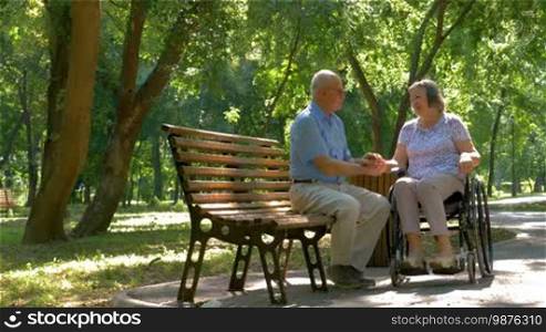 Senior man talking with woman in wheelchair outside in summer park.