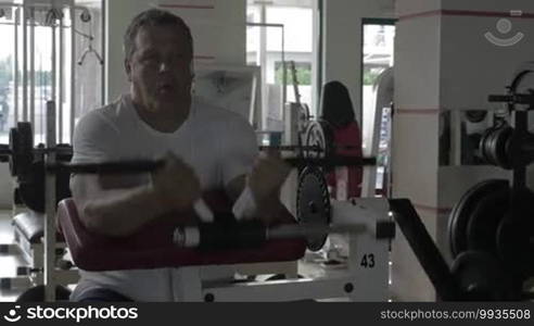 Senior man working out in the gym. He is doing bicep curl machine exercises