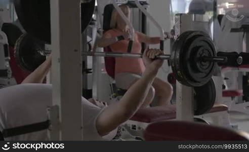 Senior people having workout in the gym. Man lifting barbell and woman exercising on chest press machine